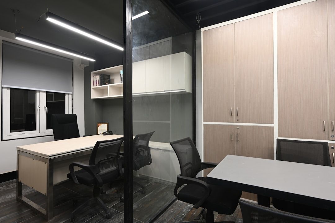 Moderne kantoorruimte met bureau, stoelen, opbergkasten en glazen scheidingswanden, netjes georganiseerd.